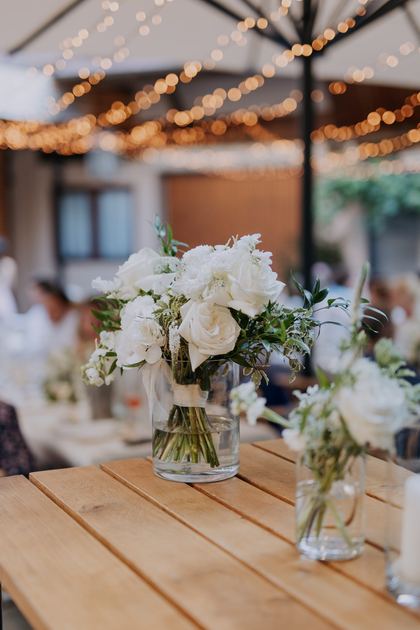 Weiße Blumen in Vasen auf der Festtafel unter Lichterketten