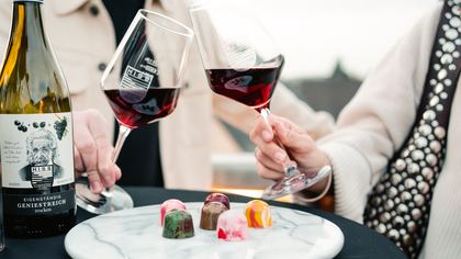 Zwei Gäste stoßen mit Rotwein über einem Menüteller an