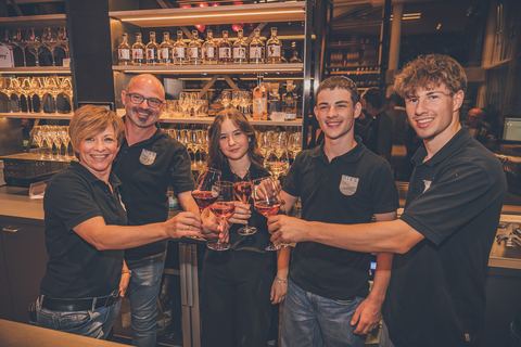 Fünf Mitglieder des Teams stoßen an der Theke der Vinothek mit Weingläsern an